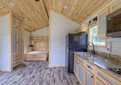 Frontier model home kitchen with a black refrigerator, stove top, and microwave over. A platform bed in the bedroom is partially visible.